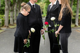 Trauernde mit Rosen auf Friedhof bei halbanonymen Gräbern